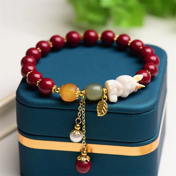 Natural cinnabar bracelet with hand-carved rabbit charm and metallic accents in deep purple-red colour