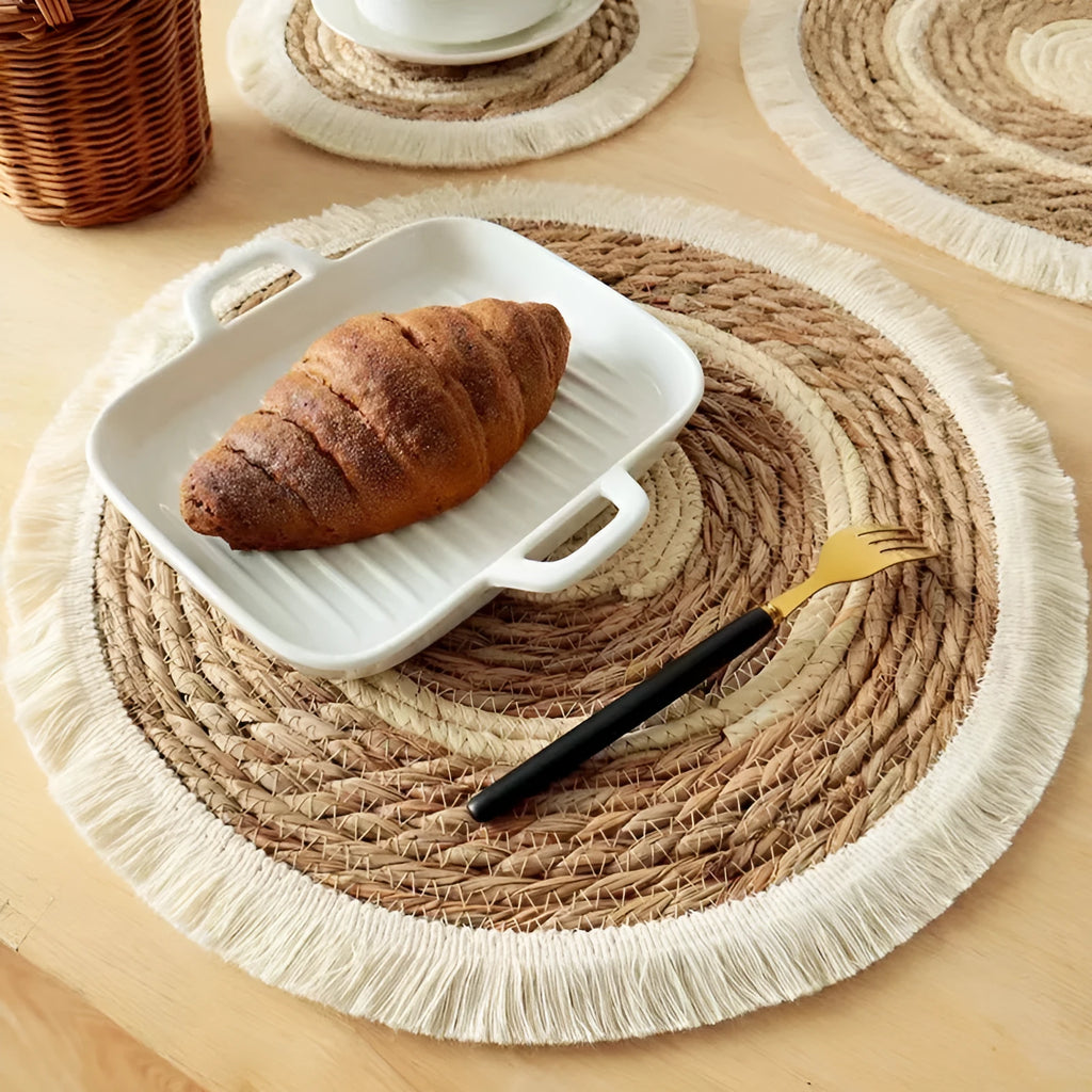 Round natural papyrus straw placemat with tassel detailing on a table.