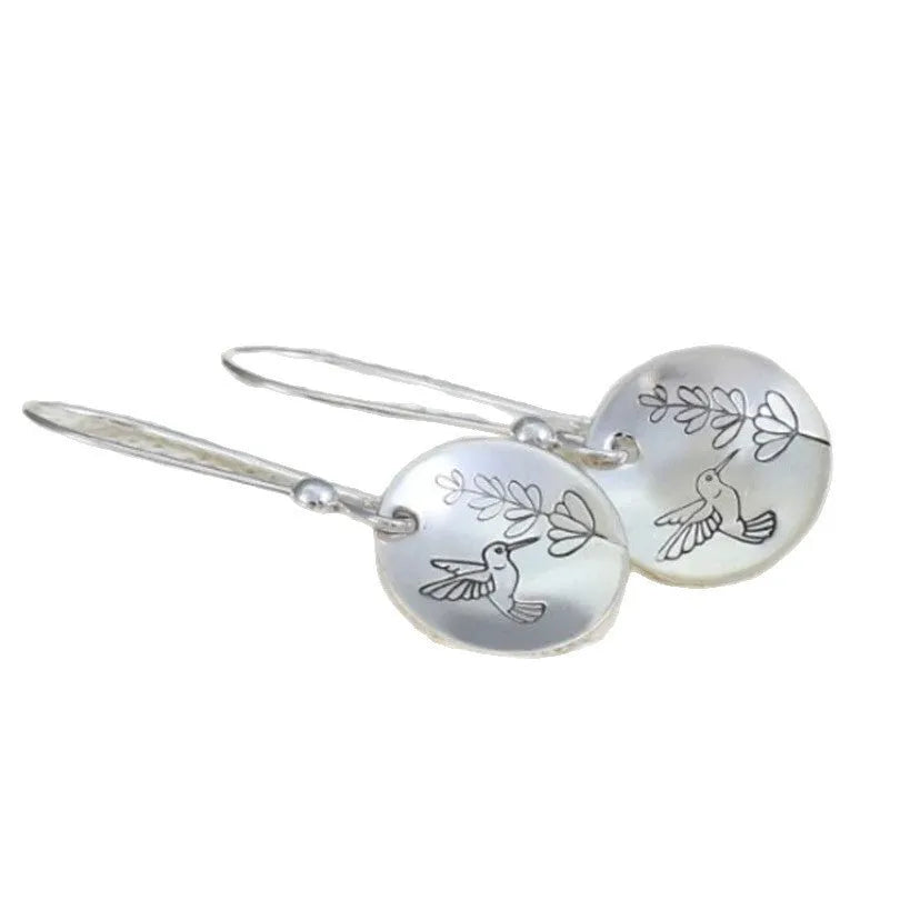 Close-up of glossy silver women's earrings with detailed bird and floral motifs on a round base.