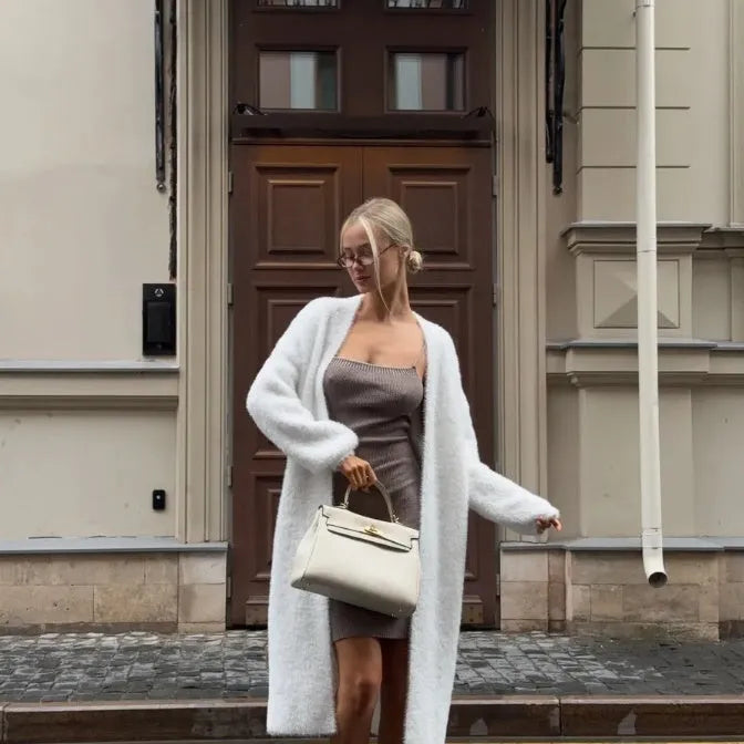 White loose-fit knitted cardigan jacket with long sleeves on a hanger.