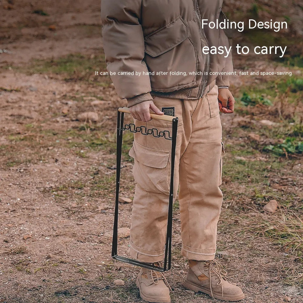 Black outdoor folding iron trash rack with wooden handle holding a rubbish bag.
