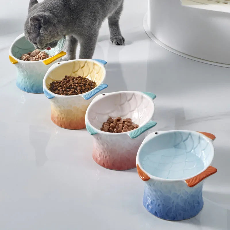 Four coloured fish-shaped ceramic pet bowls with a tilted, elevated design on a plain surface.