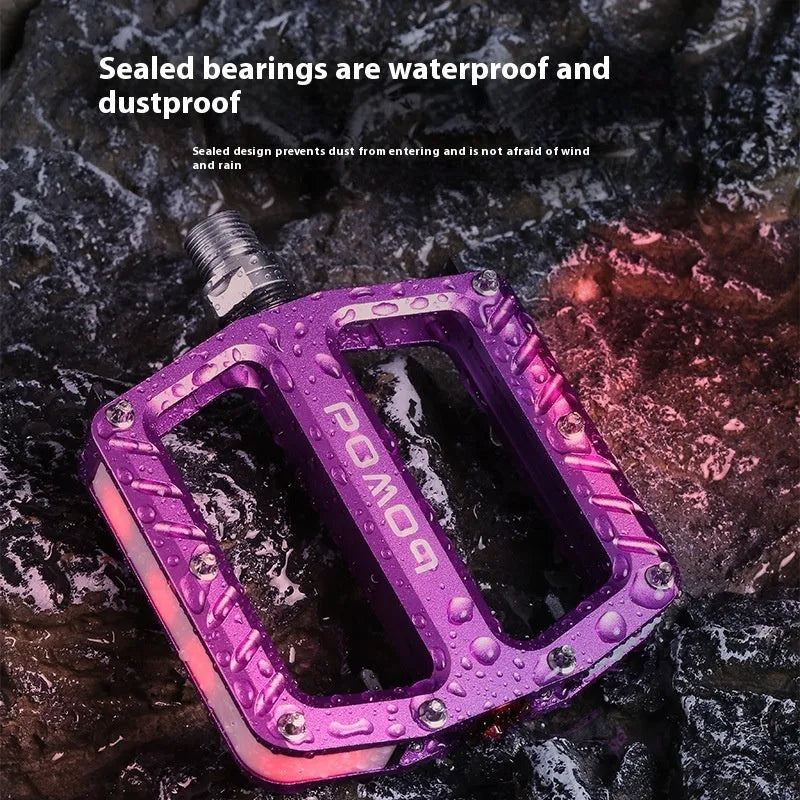 Aluminium alloy bicycle pedals with 710 LED lights in purple, black, titanium, red, and gold colours.