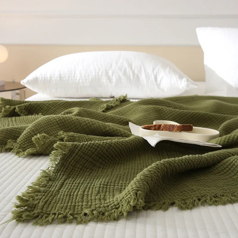 Cotton four-layer gauze blanket with tassel trim in avocado green colour on a chair.