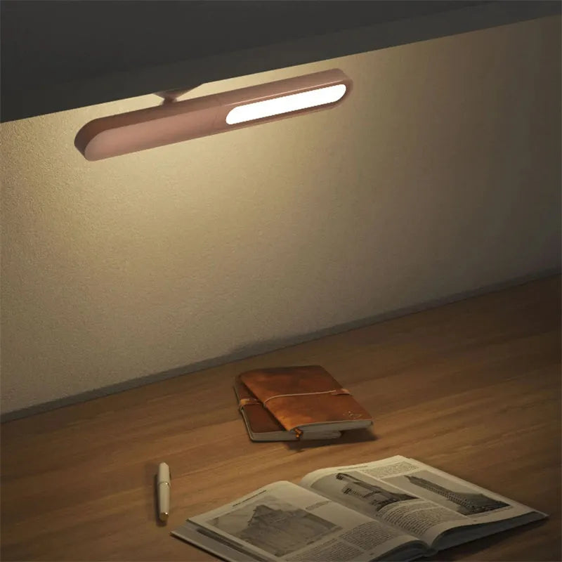 Geometric shaped white desk lamp with a magnetic base on a wooden table next to a book.