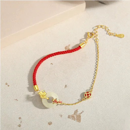 Gold and red women's bracelet with a silver peace buckle, red rope, and Hetian jade charm.