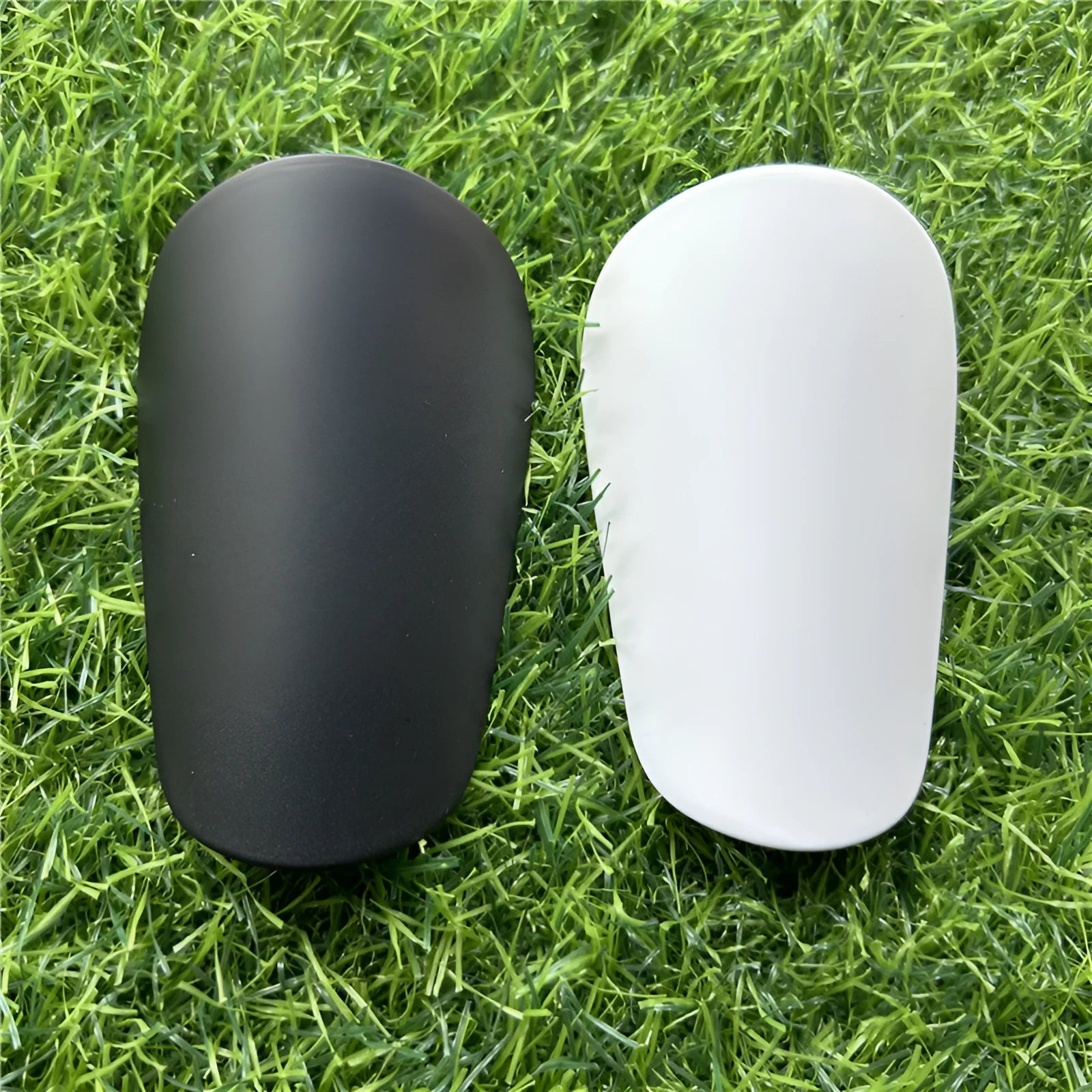 Extra small mini plastic football shin guards for kids in black and white, measuring 8 by 5 centimetres.