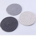 Three round cotton cord coasters in coordinating colours on wooden table