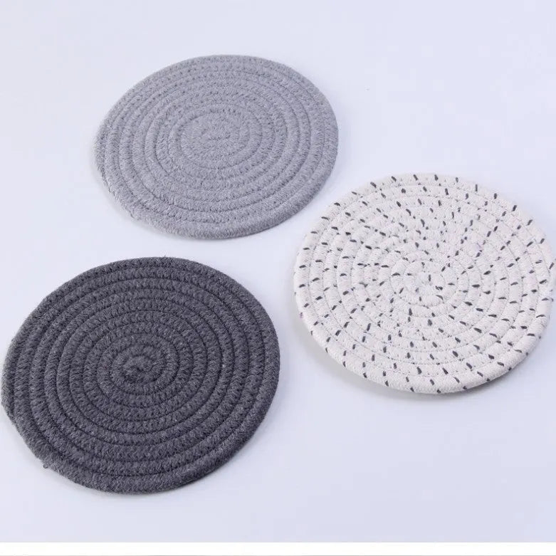 Three round cotton cord coasters in coordinating colours on wooden table