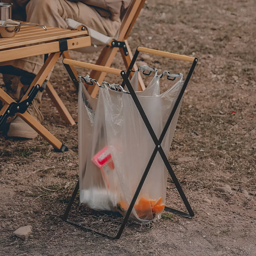 Black outdoor folding iron trash rack with wooden handle holding a rubbish bag.