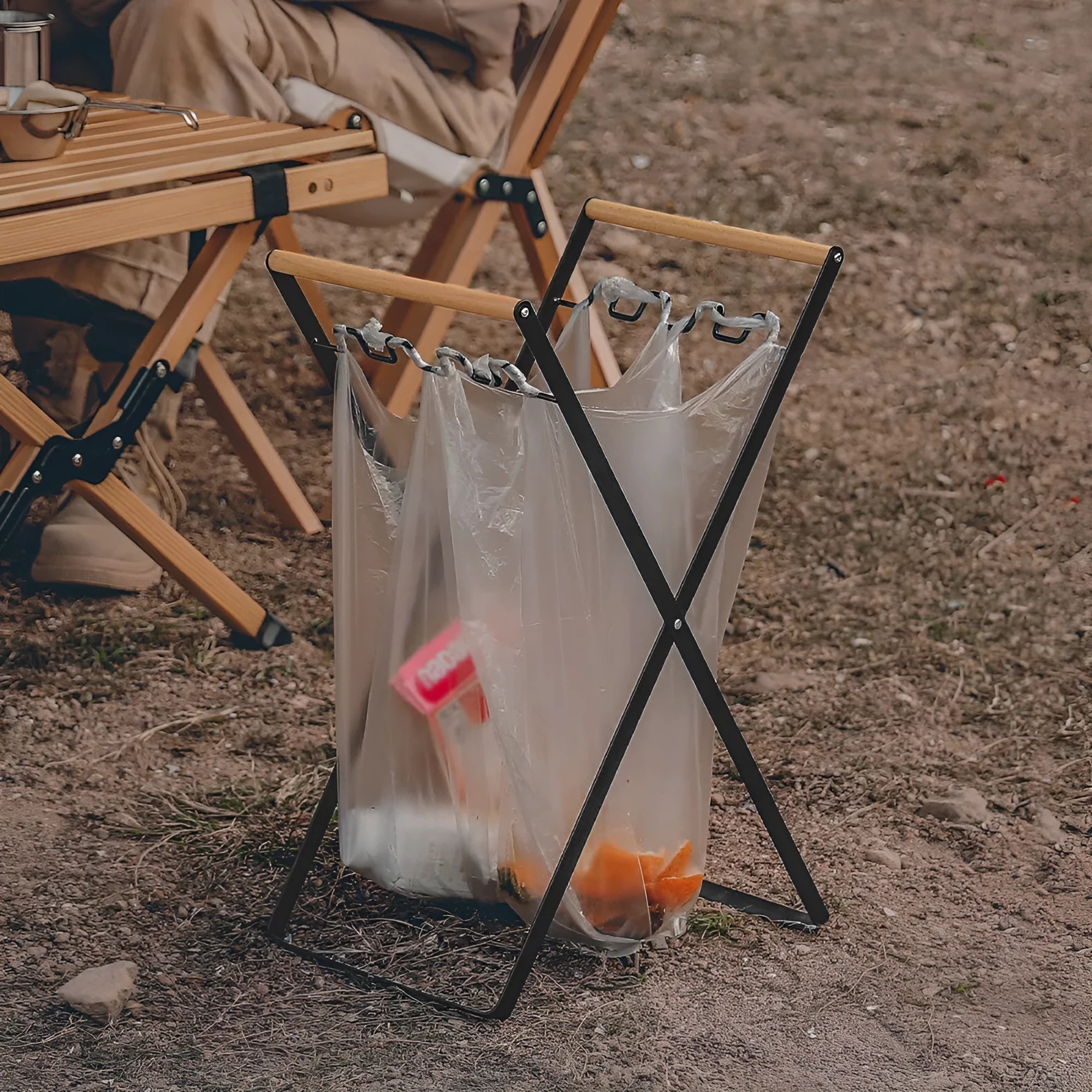 Black outdoor folding iron trash rack with wooden handle holding a rubbish bag.