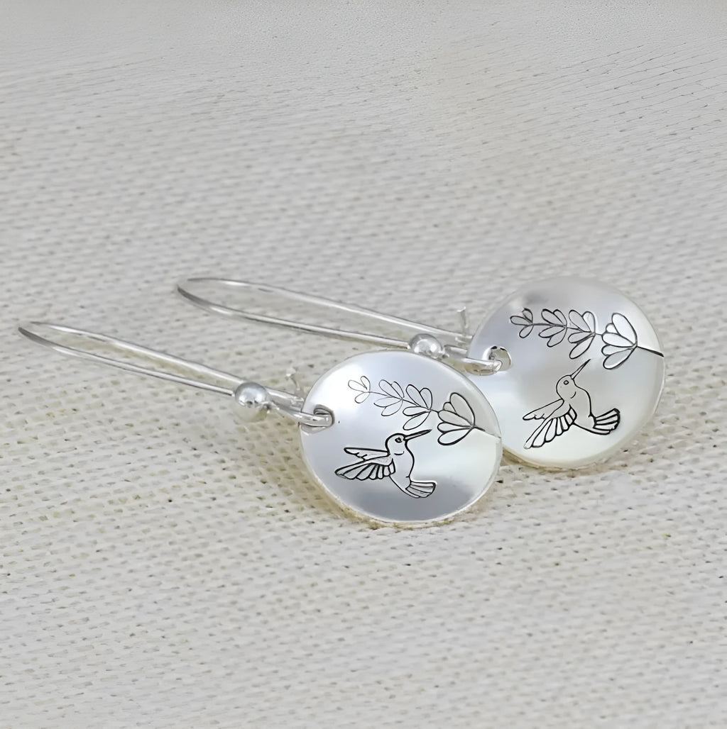 Close-up of glossy silver women's earrings with detailed bird and floral motifs on a round base.