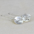 Close-up of glossy silver women's earrings with detailed bird and floral motifs on a round base.