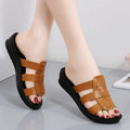 Beige women's flat-bottom slippers with waxed leather upper and soft PU sole on a wooden floor.