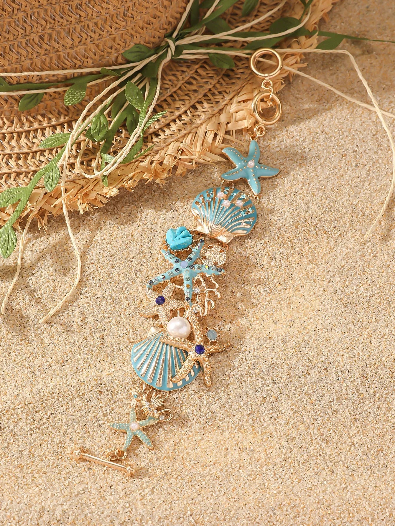 Turquoise alloy bracelet with a rhinestone boat anchor and starfish charm on a model's wrist.
