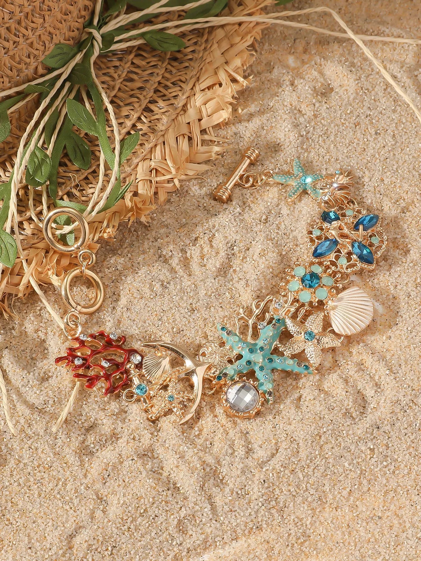Turquoise alloy bracelet with a rhinestone boat anchor and starfish charm on a model's wrist.