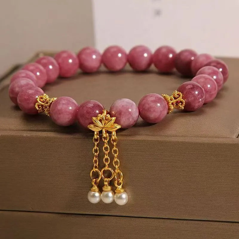 Close-up of a women's natural stone bracelet with a pink lotus tassel and pink white crystal electroplated flower pendant.