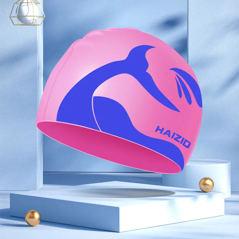 Silicone swimming cap with waterproof ear covers and a whale tail pattern in assorted colours.