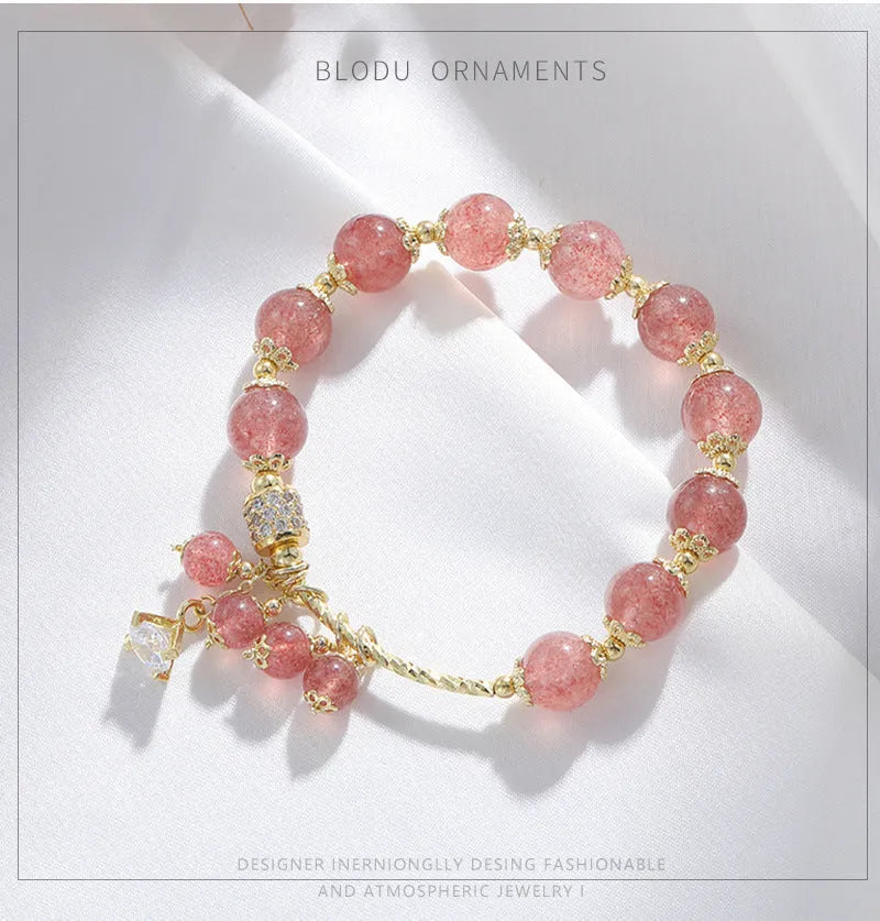 Close-up of a women's pink crystal bracelet with a heart-shaped Strawberry Quartz stone and a white pearl accent.