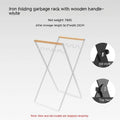Black outdoor folding iron trash rack with wooden handle holding a rubbish bag.