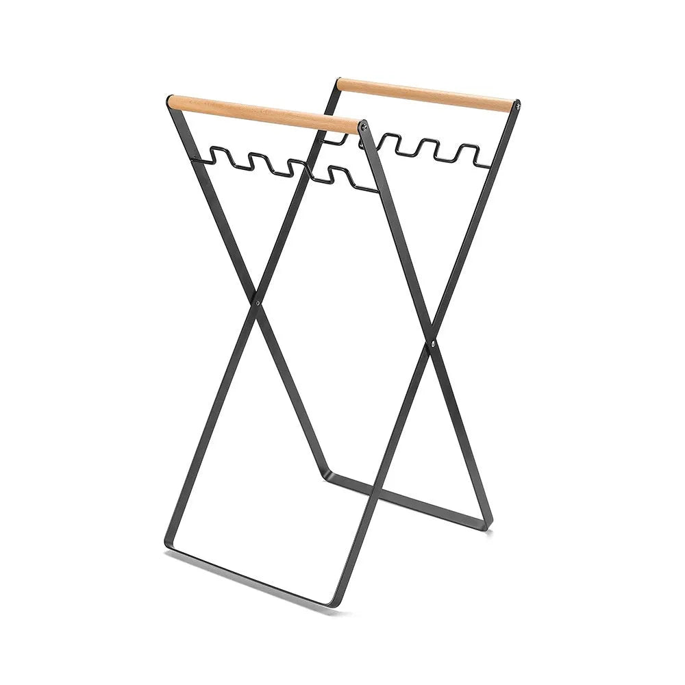 Black outdoor folding iron trash rack with wooden handle holding a rubbish bag.