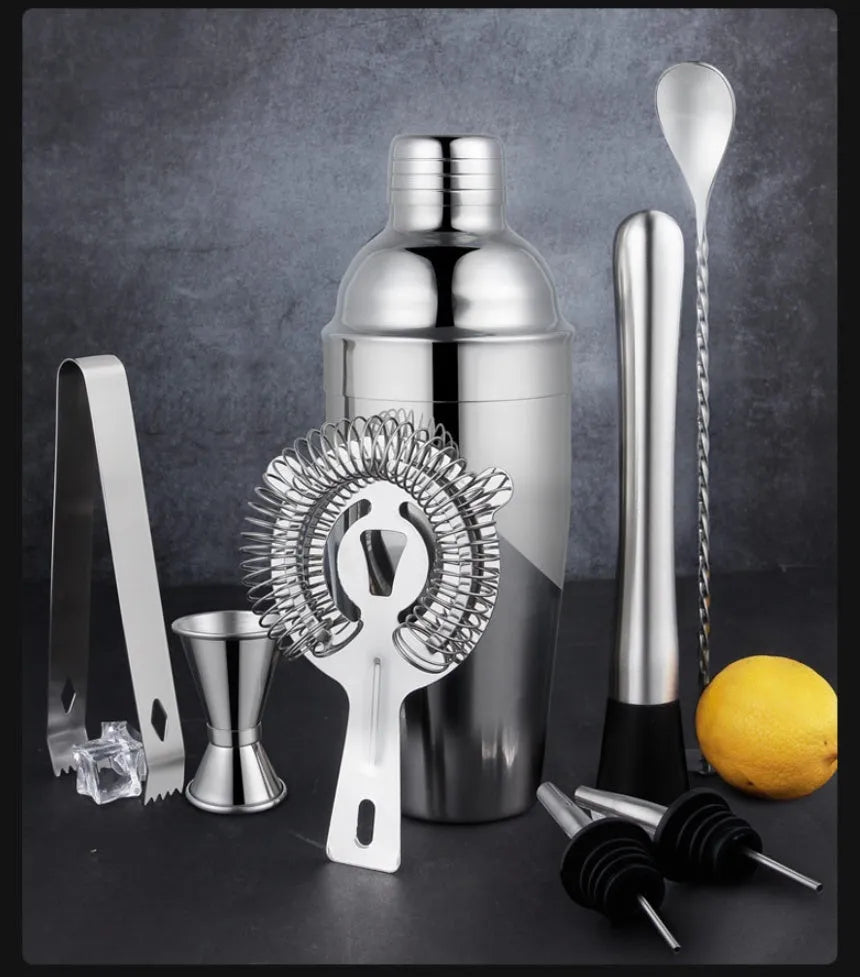 23-piece stainless steel and acrylic cocktail set with shaker, bar spoons, and strainers on a wooden bar.