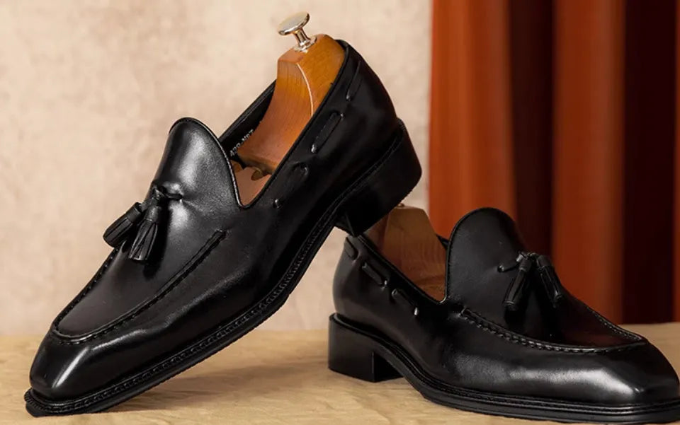 Men's black genuine leather slip-on loafers with fringe detail and rubber sole.
