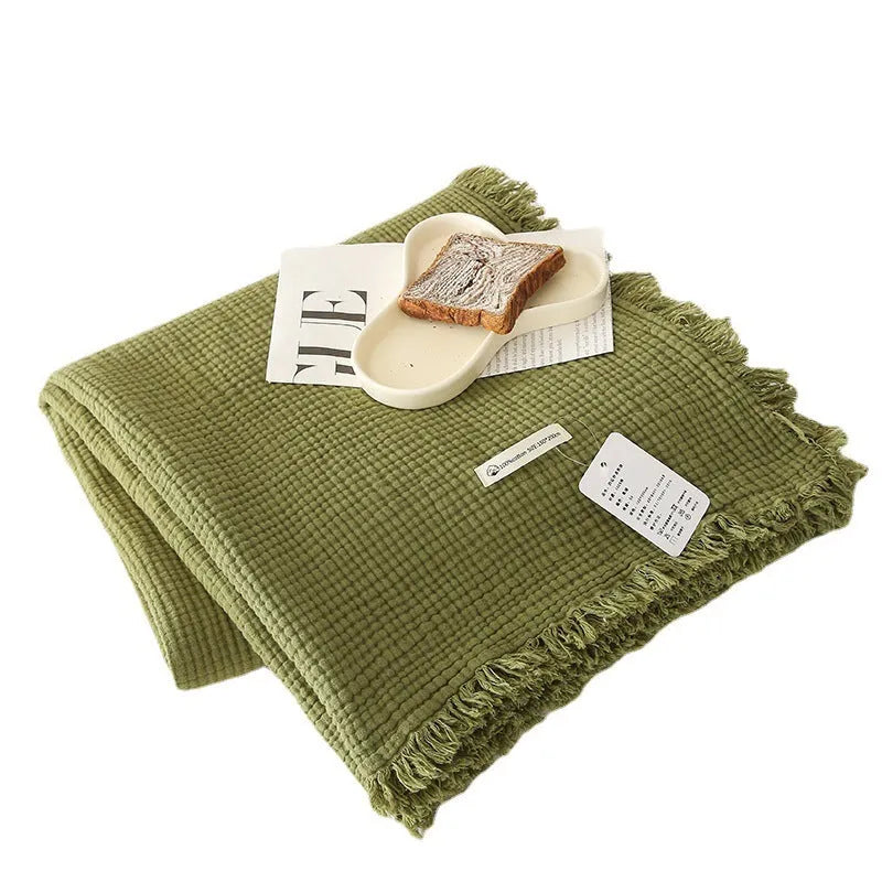 Cotton four-layer gauze blanket with tassel trim in avocado green colour on a chair.