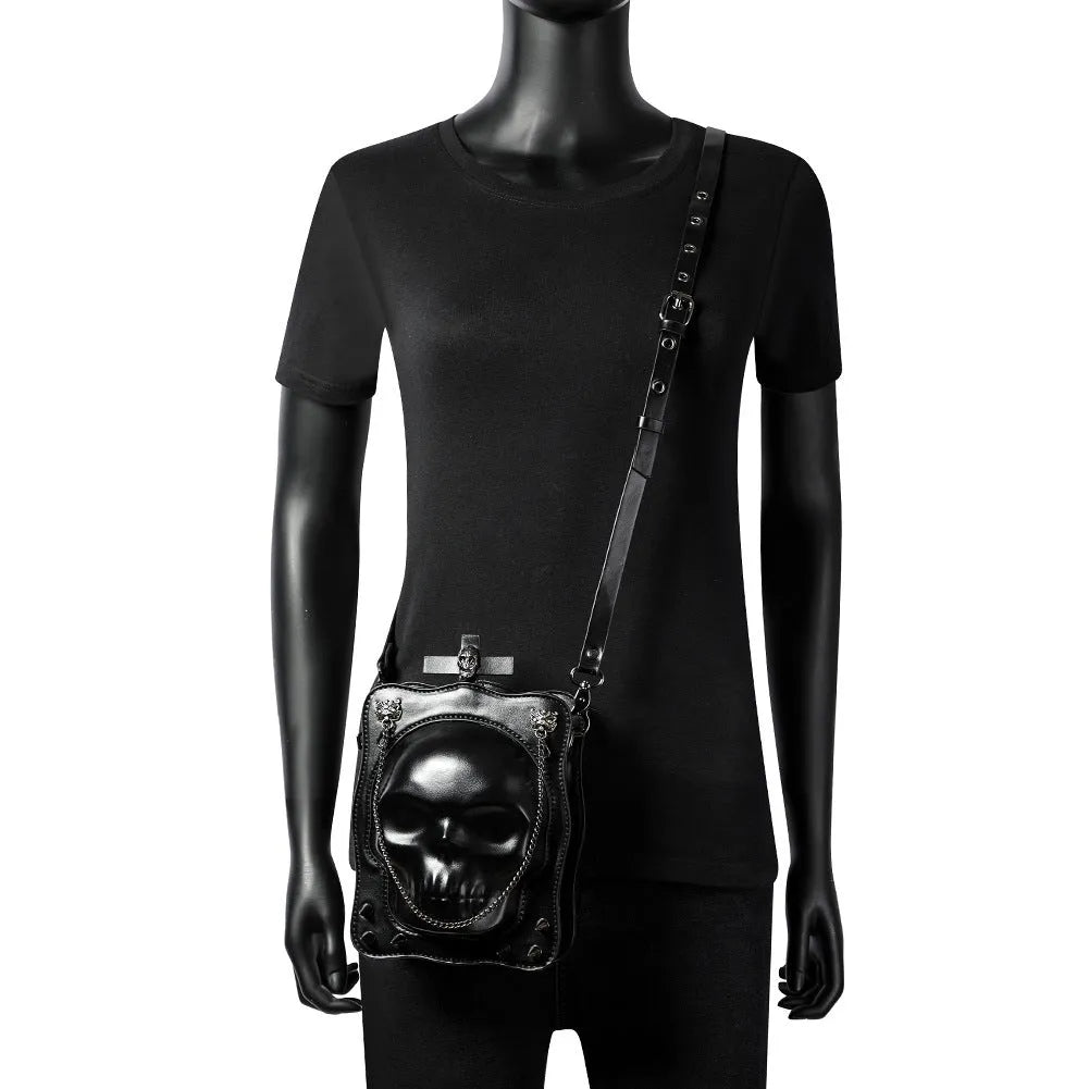 Black gothic mini square messenger bag with skull embossing, stitching, rivets, and chain details on textured PU polyester