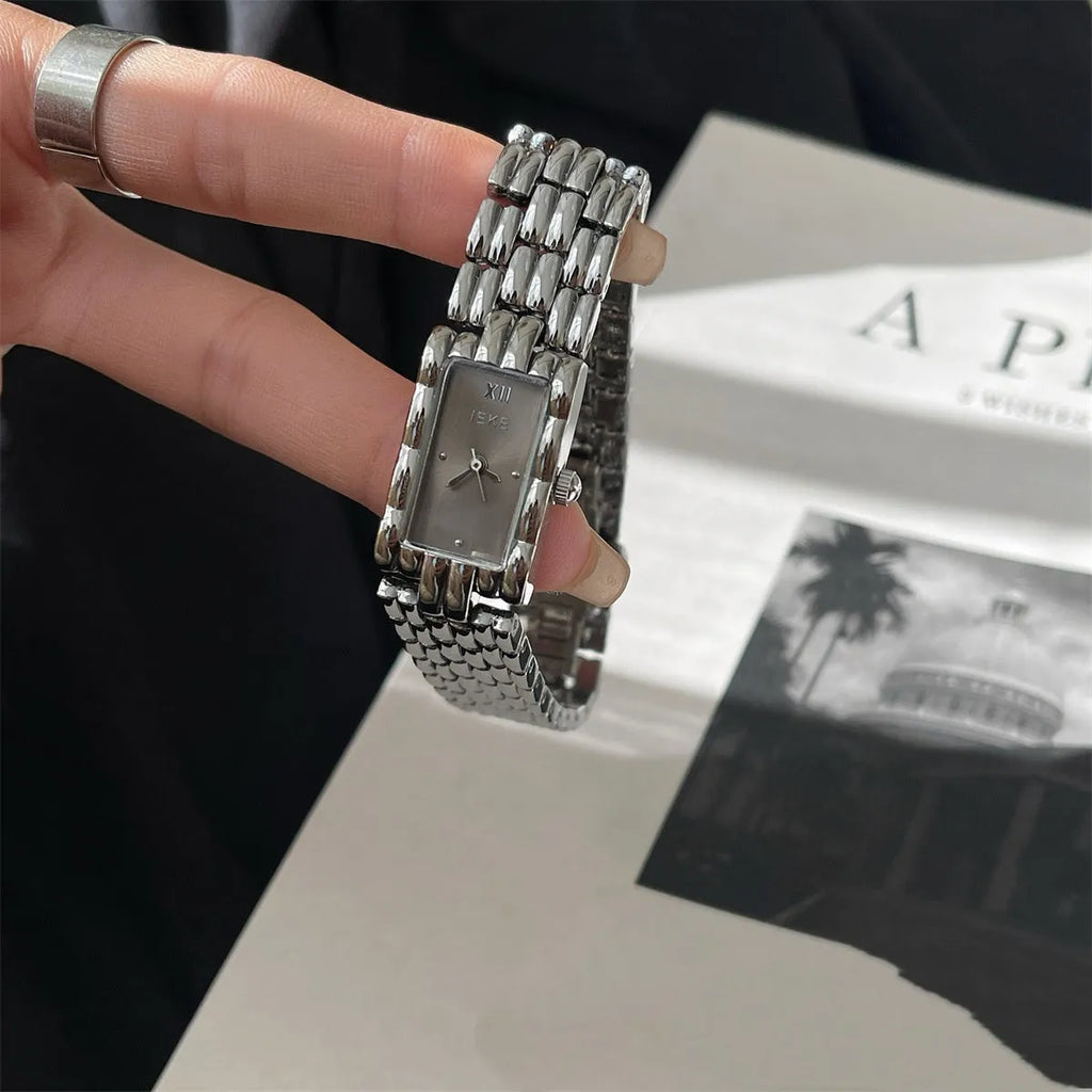 Women's antique-style bracelet watch with small white dial on a silver strap, showing butterfly buckle.