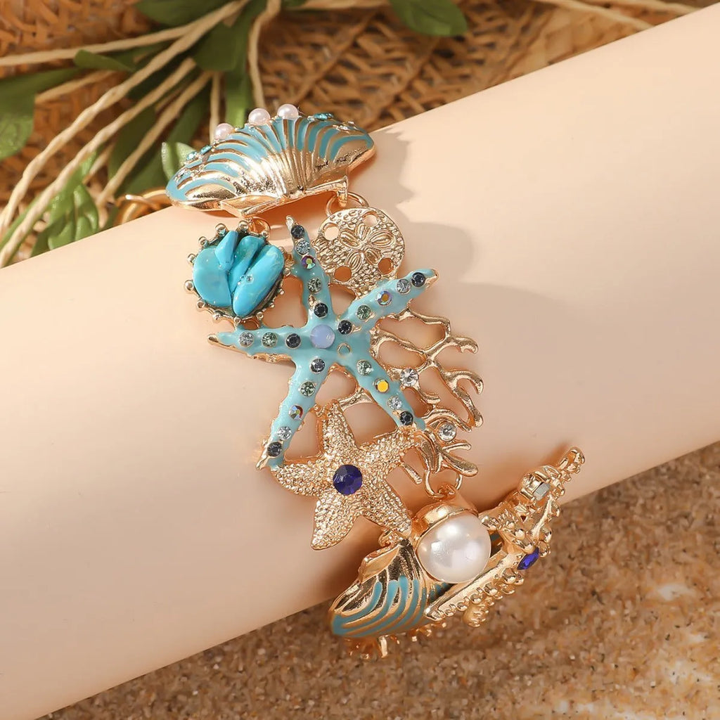 Turquoise alloy bracelet with a rhinestone boat anchor and starfish charm on a model's wrist.