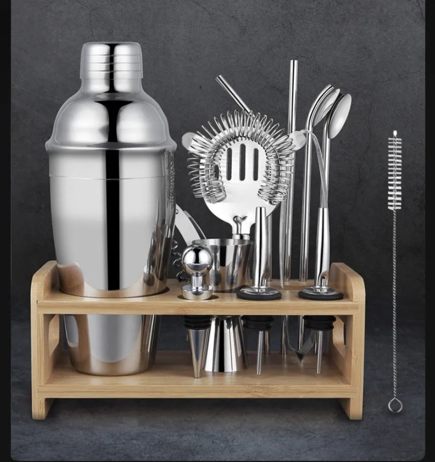 23-piece stainless steel and acrylic cocktail set with shaker, bar spoons, and strainers on a wooden bar.