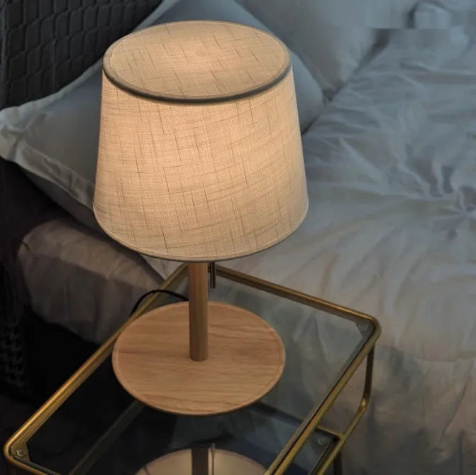 Walnut coloured solid wood desk lamp with a white cloth lampshade and a black cable switch.