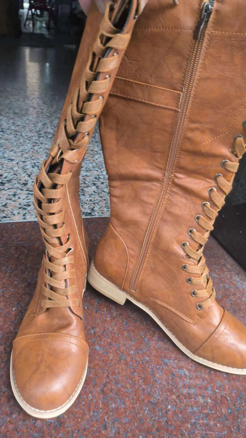 Black women's knee high boots with cross strap and lace-up front design on a white background.