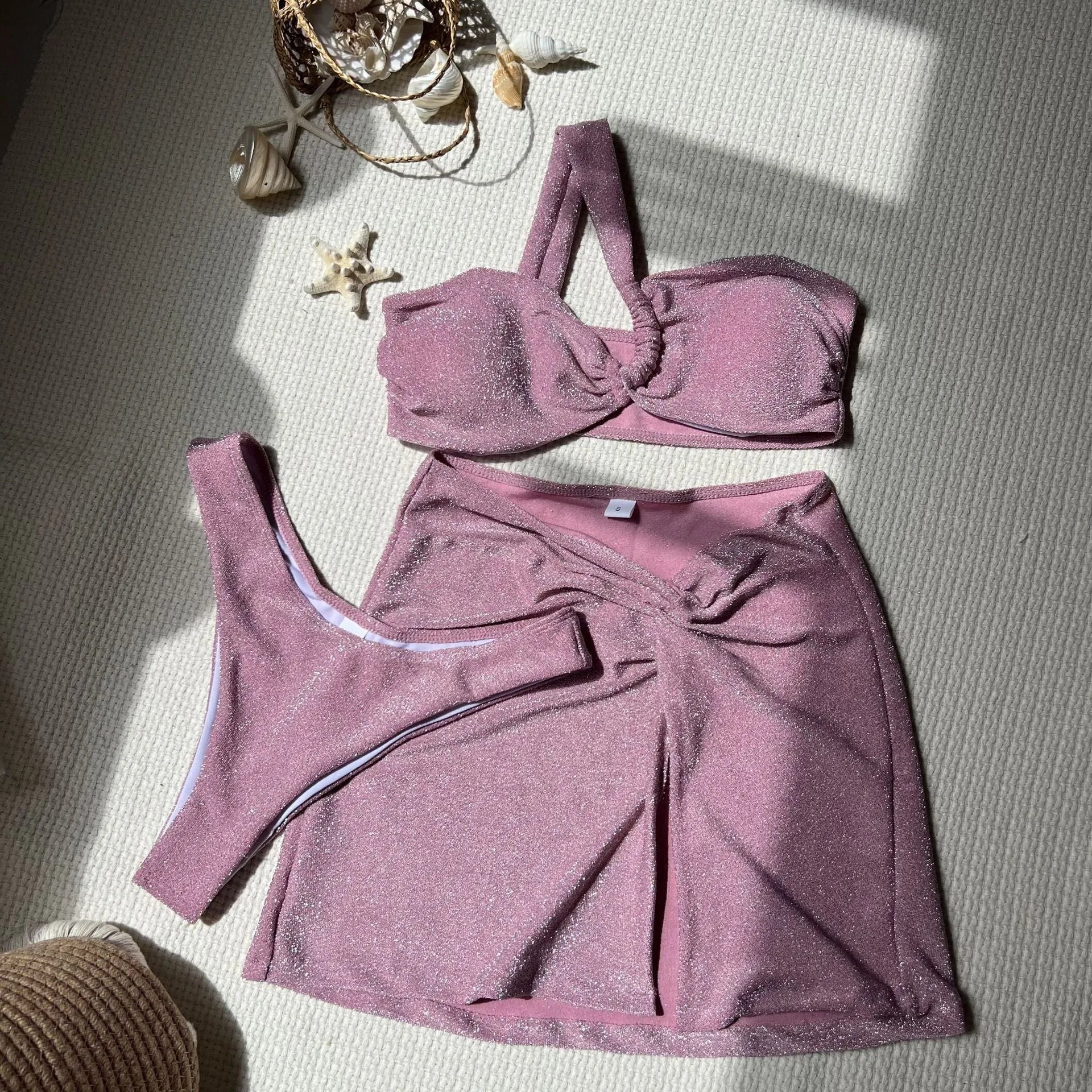 Women's glossy one-shoulder three-piece swimsuit set in light green, including top, pants, and skirt.