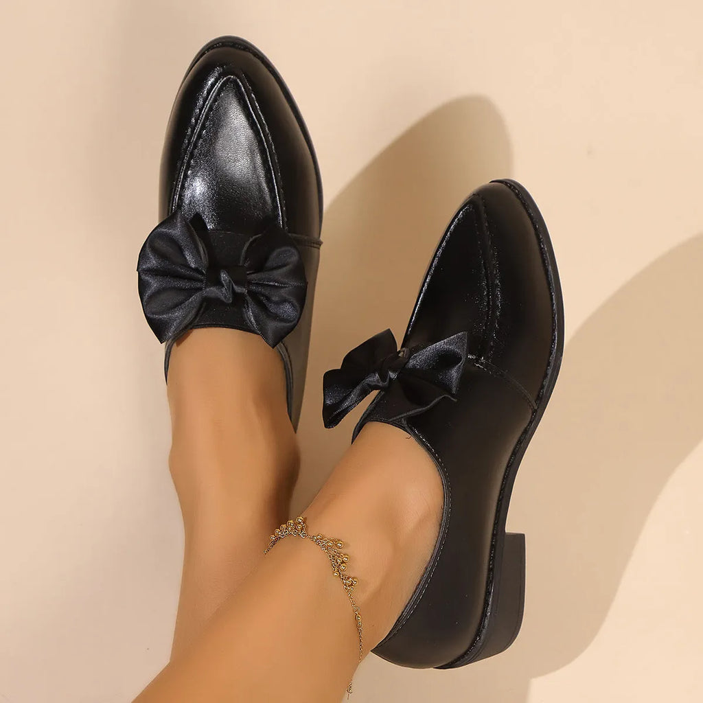 Women's brown leather-look loafers with a large bow detail on the front.