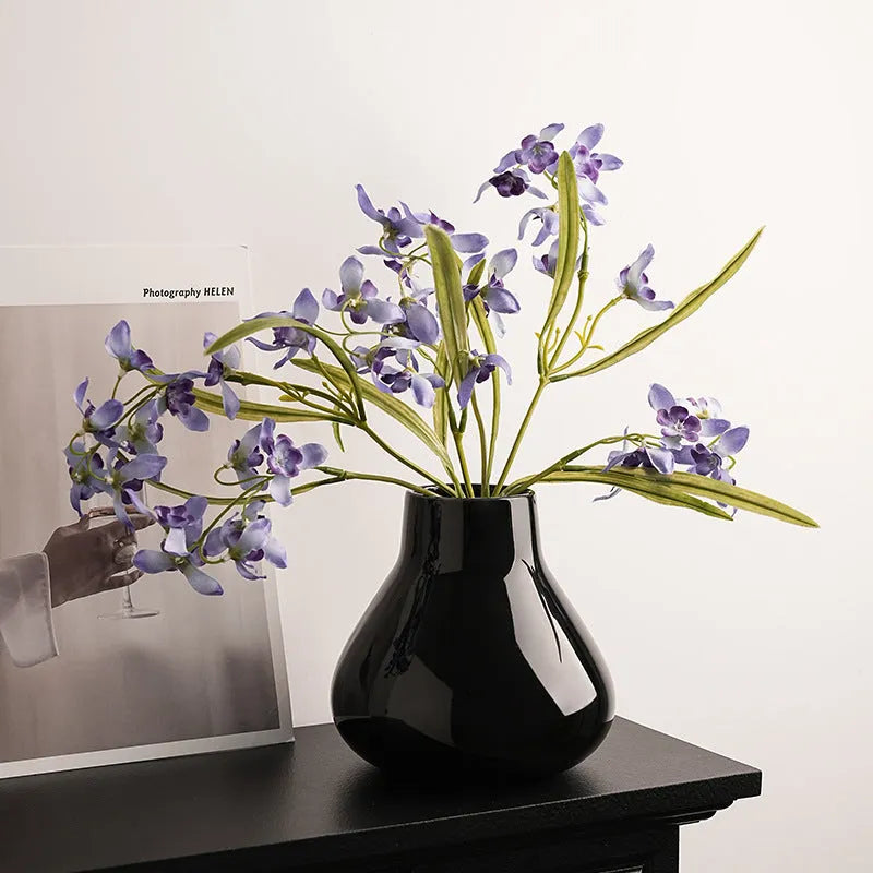 Black ceramic modern vase with white artificial orchid stems on wooden table