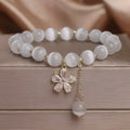 Women's single loop white cat's eye crystal bracelet with flower pattern and tassels, showing safety buckle clasp
