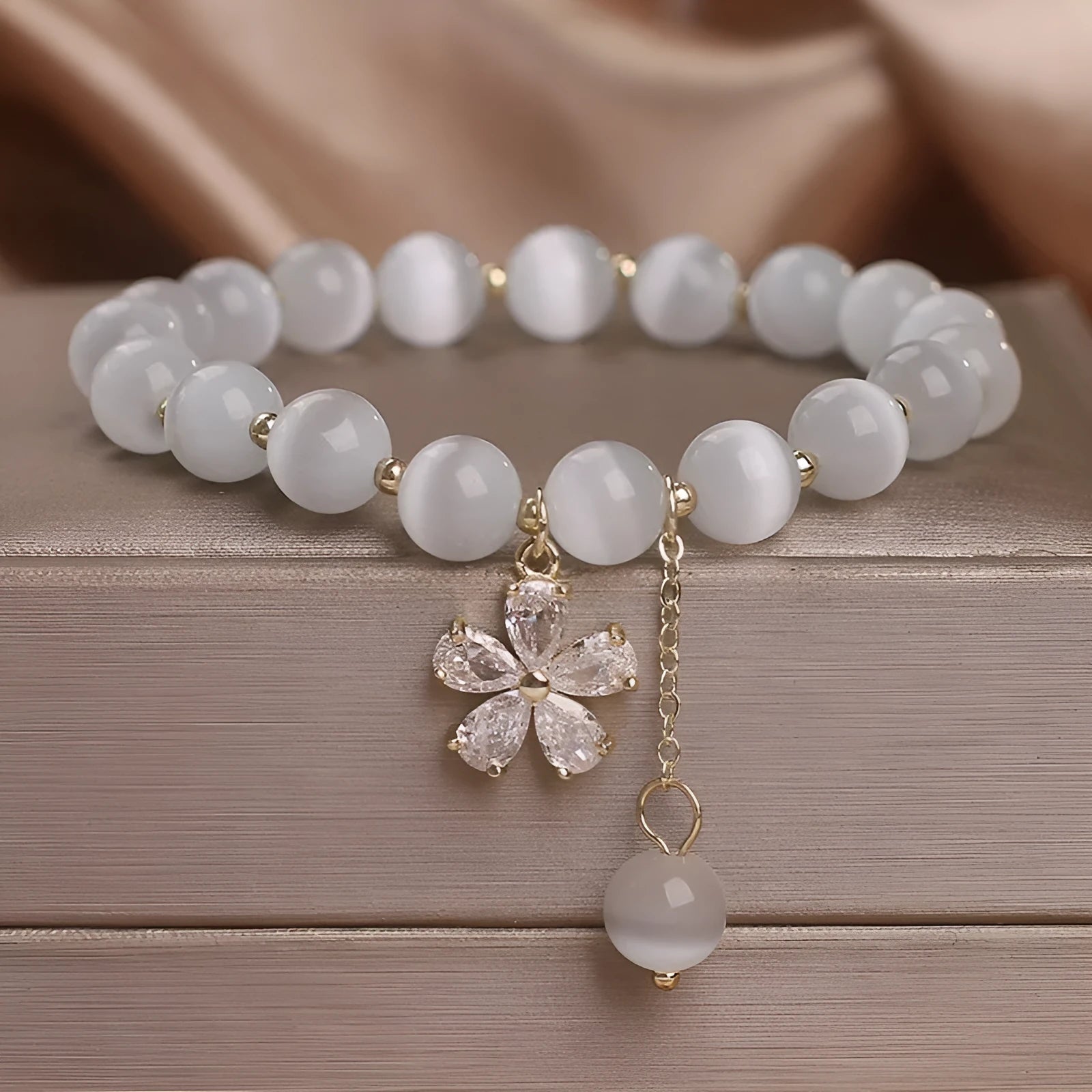 Women's single loop white cat's eye crystal bracelet with flower pattern and tassels, showing safety buckle clasp