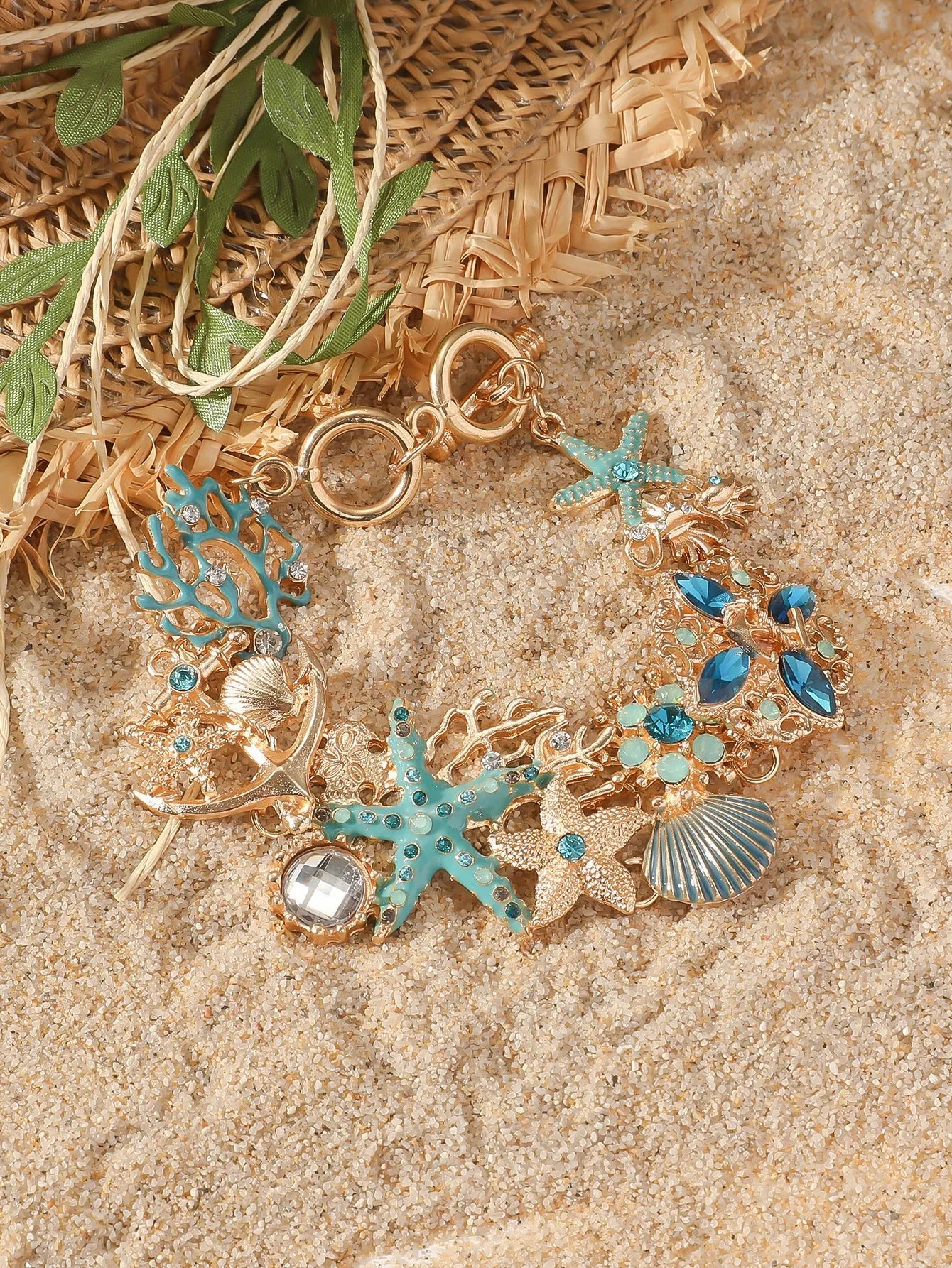 Turquoise alloy bracelet with a rhinestone boat anchor and starfish charm on a model's wrist.