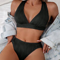 Women's black halter strap bikini with split shorts design on size chart background