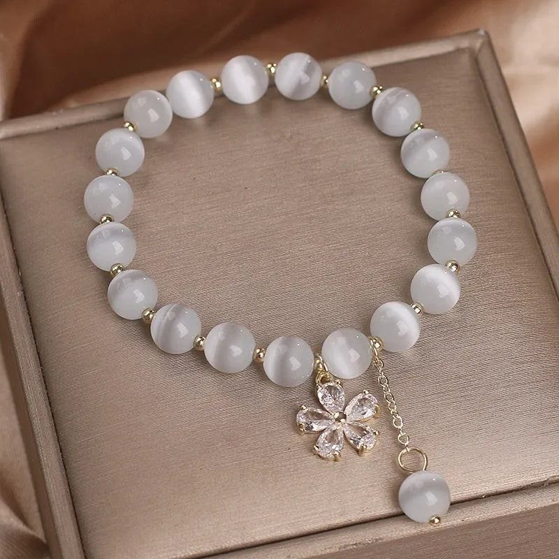 Women's single loop white cat's eye crystal bracelet with flower pattern and tassels, showing safety buckle clasp