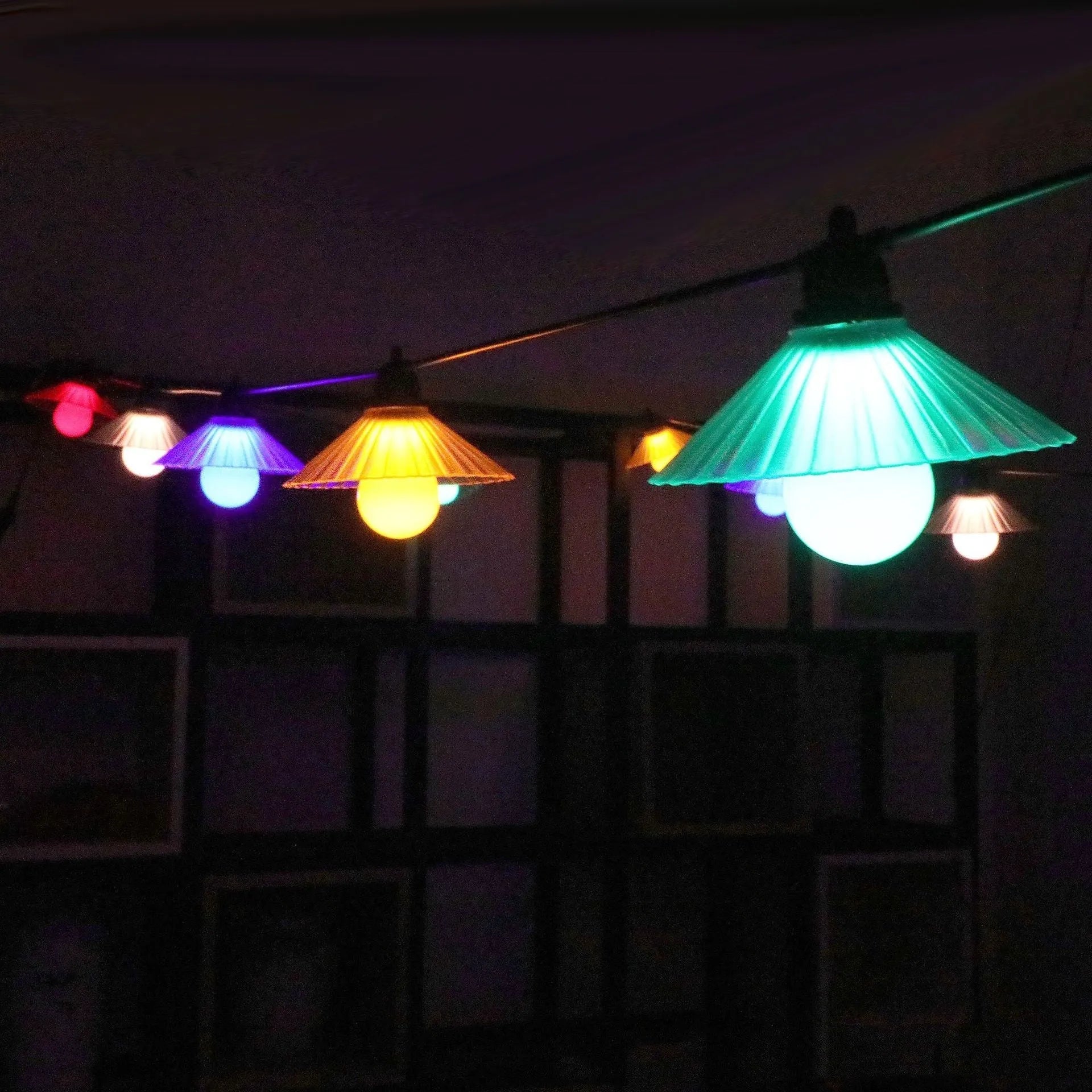 Outdoor LED string lights with flower-shaped white globes hung on a garden fence.