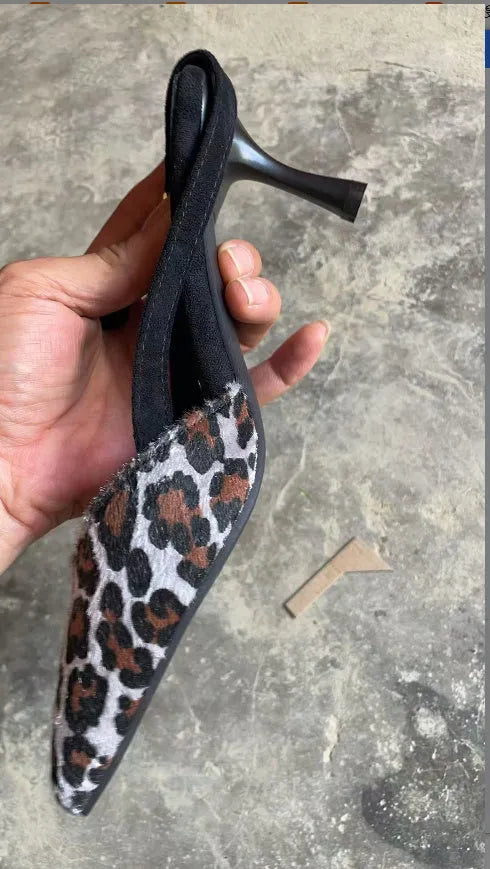 Women's leopard print suede sandals with a pointed toe and high heel on a plain background.