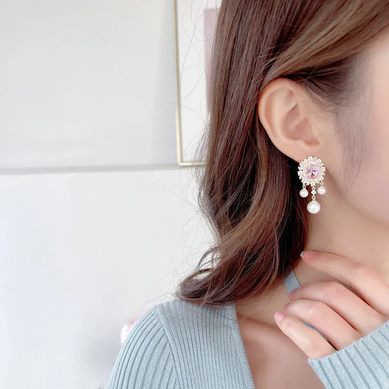 A pair of oval-shaped geometric drop earrings with a pearl tassel and zircon inlay on copper, shown in light purple.