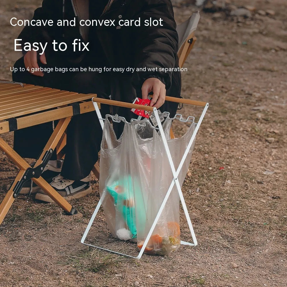 Black outdoor folding iron trash rack with wooden handle holding a rubbish bag.