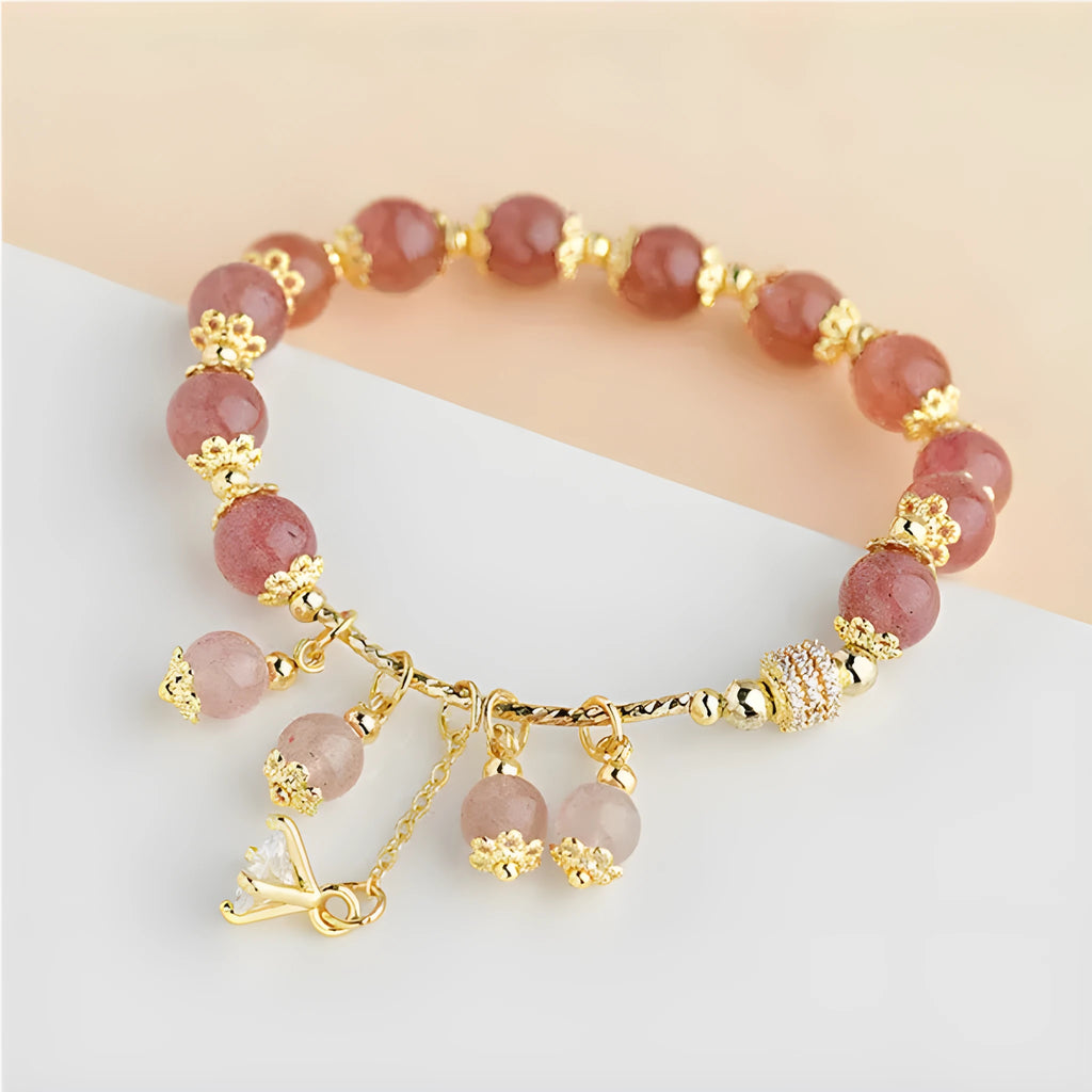 Close-up of a women's pink crystal bracelet with a heart-shaped Strawberry Quartz stone and a white pearl accent.