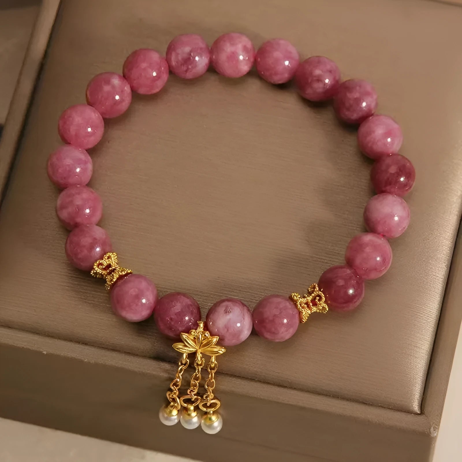 Close-up of a women's natural stone bracelet with a pink lotus tassel and pink white crystal electroplated flower pendant.